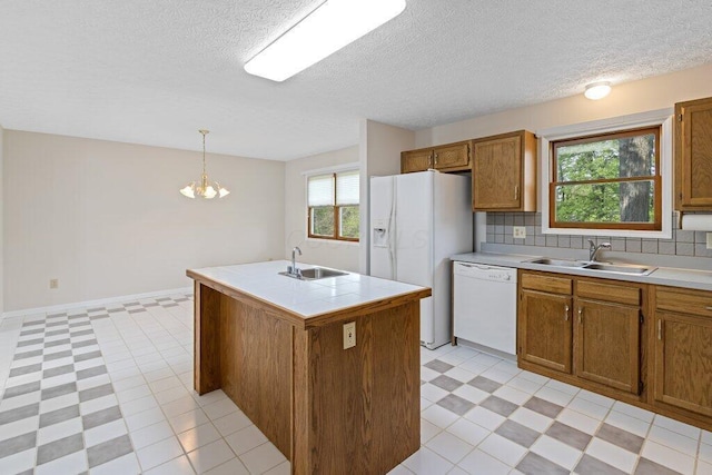 kitchen featuring a sink, white appliances, an island with sink, brown cabinetry, and a textured ceiling