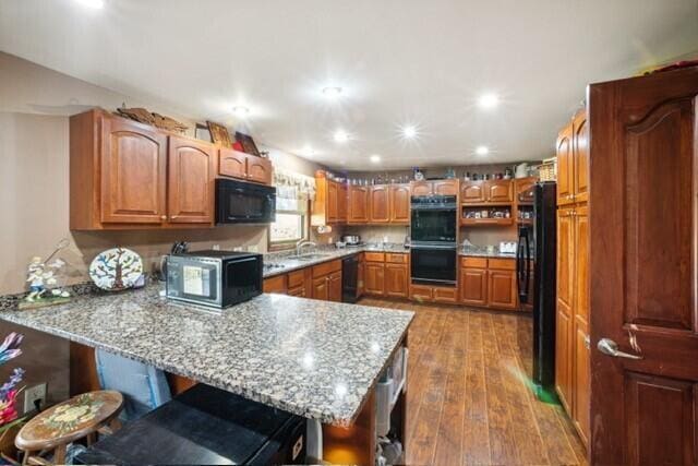 kitchen featuring a sink, a breakfast bar, black appliances, wood finished floors, and a peninsula