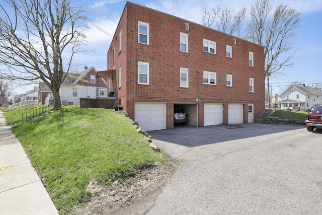 view of side of property featuring a residential view, brick siding, an attached garage, a yard, and aphalt driveway
