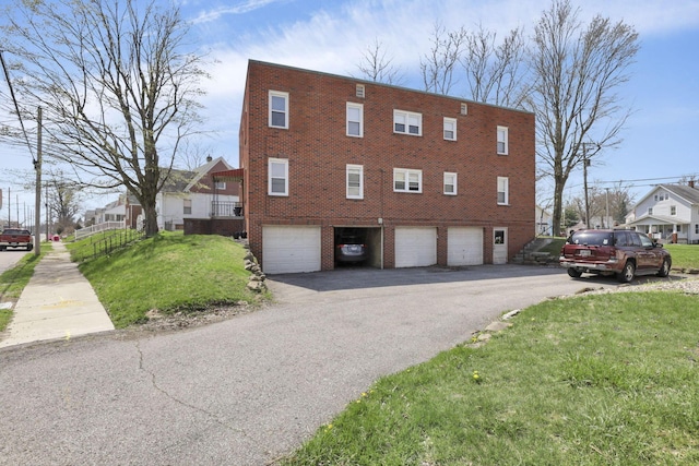 view of side of home with an attached garage, brick siding, a yard, and aphalt driveway