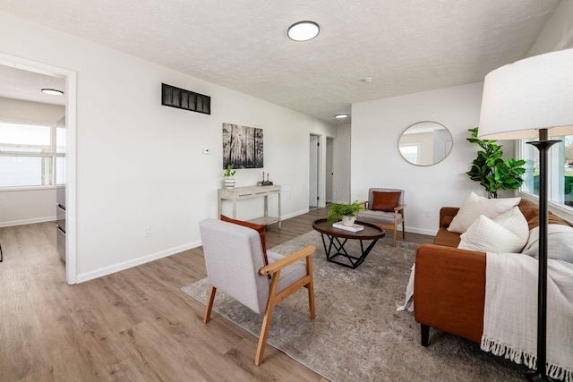 living room with light wood-type flooring, a textured ceiling, and baseboards
