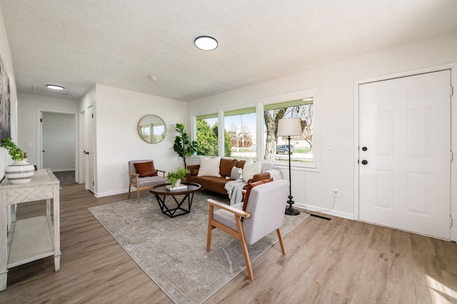 living room featuring light wood-type flooring, a textured ceiling, and baseboards