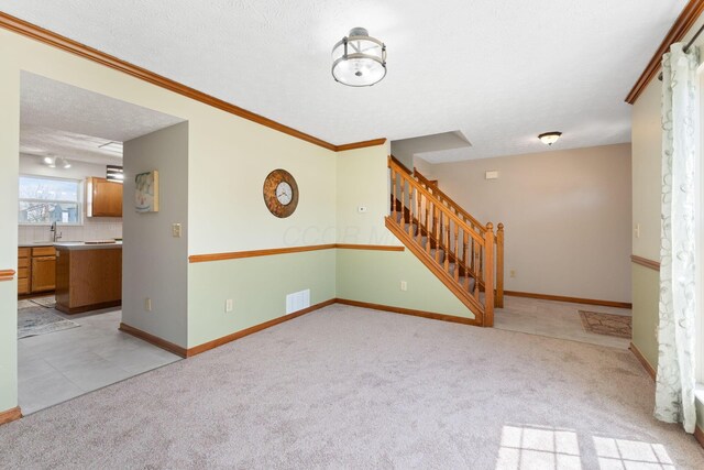 unfurnished room with stairway, light carpet, ornamental molding, and visible vents