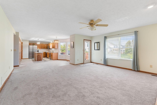 unfurnished living room with light carpet, baseboards, a textured ceiling, and ceiling fan