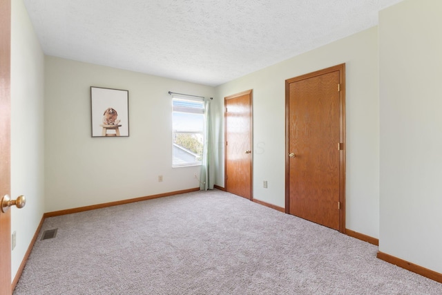 unfurnished bedroom featuring baseboards, a textured ceiling, visible vents, and carpet