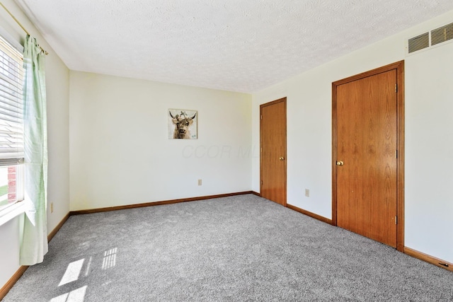 carpeted spare room with a textured ceiling, visible vents, and baseboards