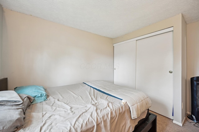 bedroom with a textured ceiling, light colored carpet, and a closet