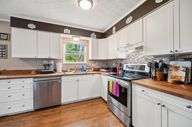 kitchen featuring butcher block counters, white cabinetry, under cabinet range hood, a sink, and stainless steel appliances