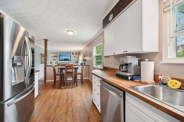 kitchen featuring plenty of natural light, appliances with stainless steel finishes, light wood-type flooring, white cabinets, and butcher block counters