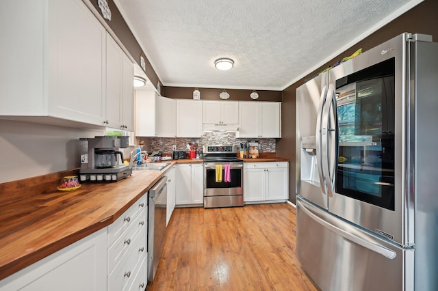 kitchen featuring a sink, wooden counters, stainless steel appliances, white cabinetry, and under cabinet range hood