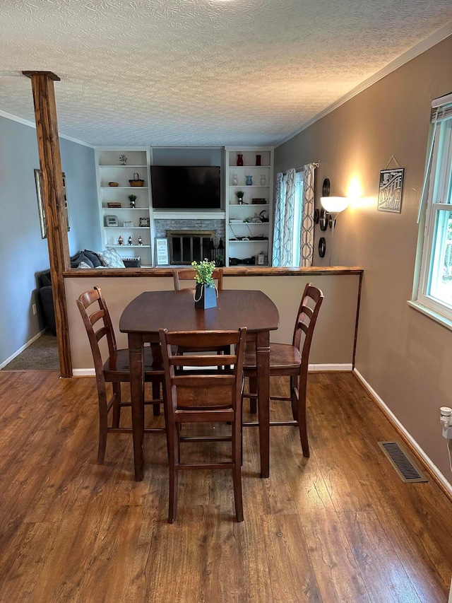 604 Forestwood Dr, Gahanna, OH 43230 - dining room featuring wood finished floors, crown molding, a textured ceiling, a glass covered fireplace, and built in features