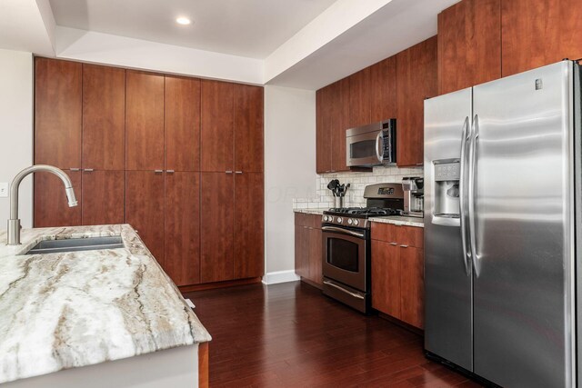 kitchen with brown cabinetry, dark wood-style flooring, tasteful backsplash, a sink, and stainless steel appliances