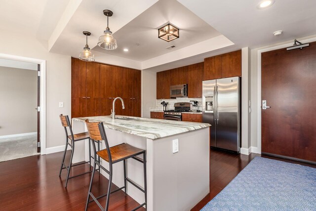 kitchen featuring brown cabinetry, a kitchen bar, a sink, stainless steel appliances, and dark wood-type flooring
