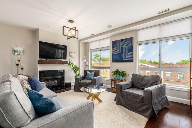 living area with visible vents, an inviting chandelier, hardwood / wood-style floors, baseboards, and a fireplace with flush hearth