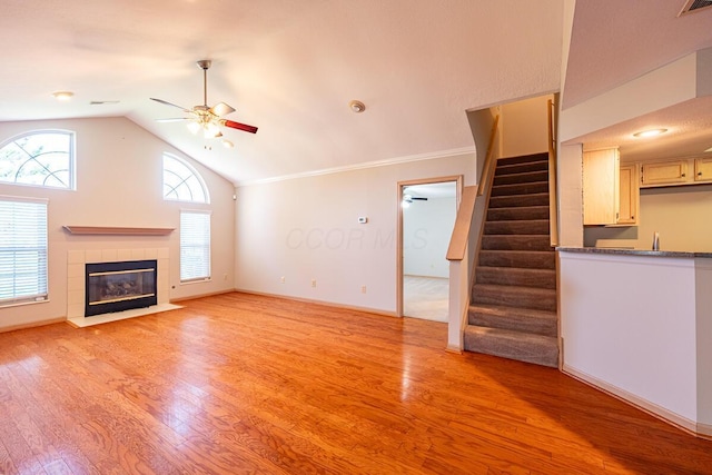 unfurnished living room with light wood-style flooring, a tiled fireplace, stairs, and ceiling fan