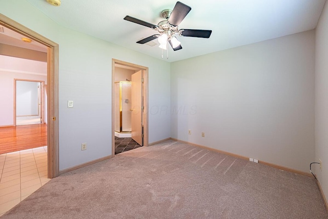 unfurnished bedroom with carpet, tile patterned floors, connected bathroom, baseboards, and ceiling fan