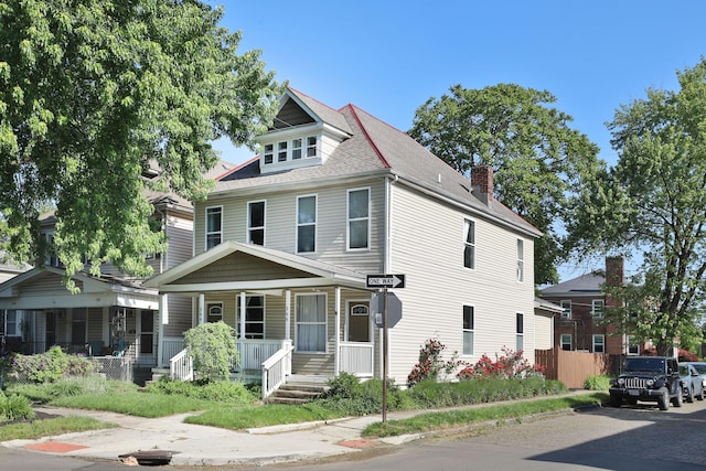 american foursquare style home with roof with shingles, a chimney, covered porch, and fence
