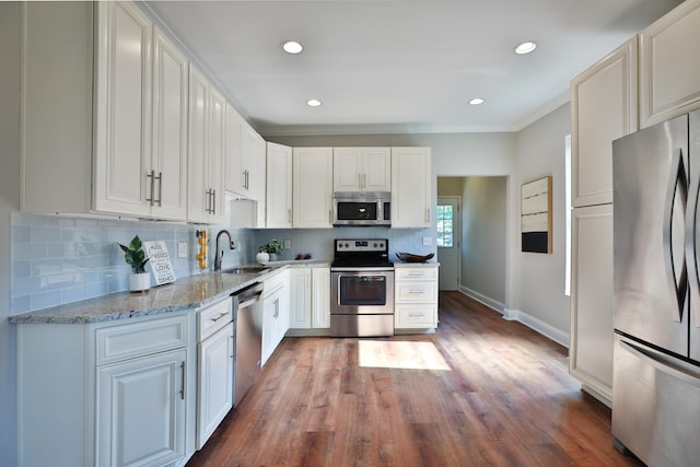 kitchen with stainless steel appliances, a sink, baseboards, decorative backsplash, and light stone countertops