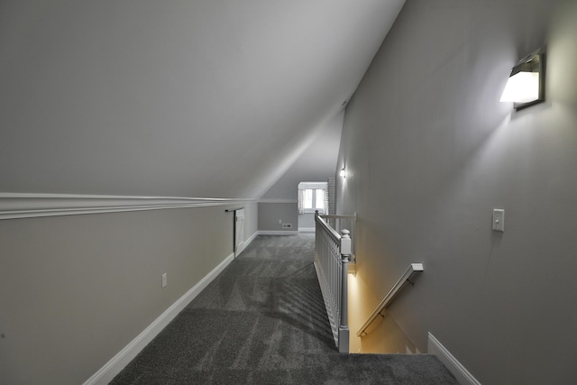 corridor with dark carpet, baseboards, an upstairs landing, and lofted ceiling