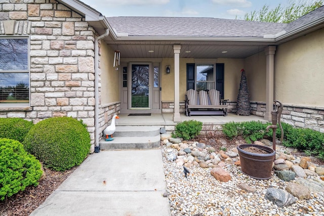 doorway to property with stone siding, a shingled roof, and a porch
