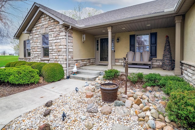 doorway to property with covered porch, stone siding, stucco siding, and a shingled roof