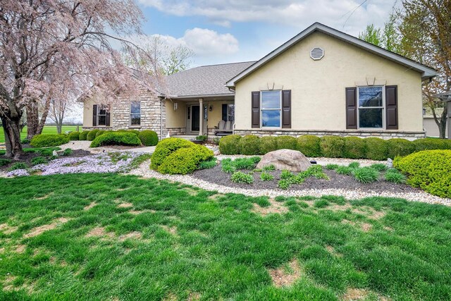 ranch-style house featuring stone siding, covered porch, a front yard, and stucco siding