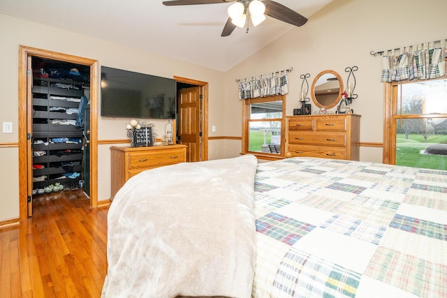 bedroom with vaulted ceiling, wood finished floors, a ceiling fan, a walk in closet, and a closet