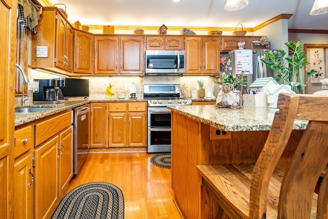 kitchen with brown cabinetry, ornamental molding, stainless steel appliances, and light wood finished floors