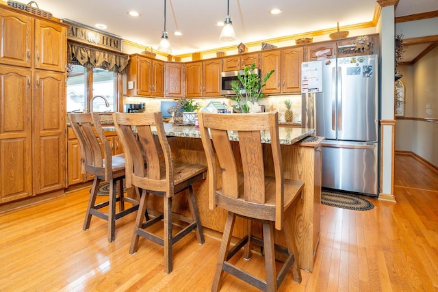 kitchen with light wood finished floors, stainless steel appliances, a center island, brown cabinetry, and ornamental molding