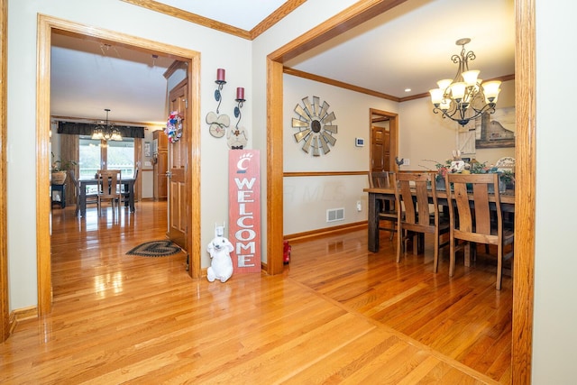 hall featuring a notable chandelier, crown molding, visible vents, and light wood-style flooring
