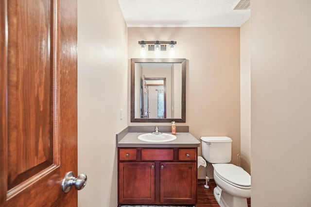 half bath with baseboards, visible vents, vanity, and toilet