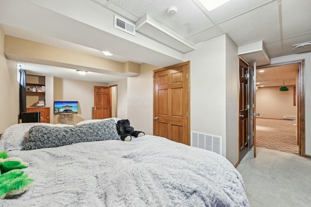 bedroom featuring baseboard heating, a drop ceiling, visible vents, and carpet