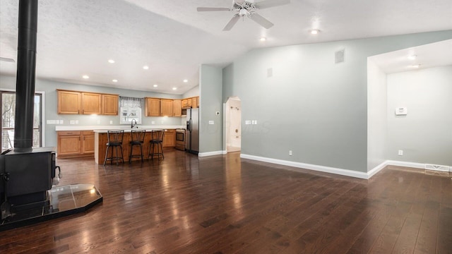 unfurnished living room with dark wood-style floors, visible vents, lofted ceiling, a ceiling fan, and a wood stove