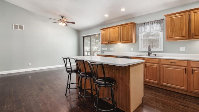 kitchen featuring a sink, visible vents, a ceiling fan, light countertops, and a breakfast bar