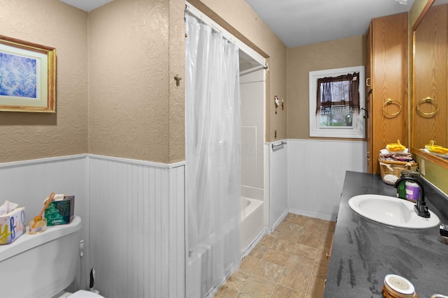 full bathroom with toilet, vanity, shower / tub combo with curtain, stone finish flooring, and wainscoting