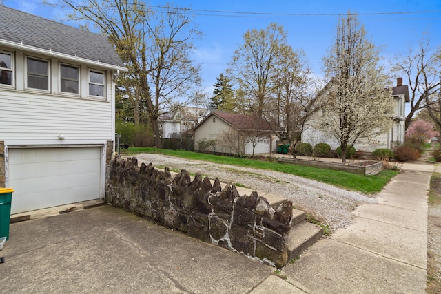 view of side of home featuring an attached garage, driveway, and roof with shingles