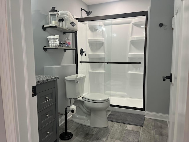 bathroom featuring a stall shower, toilet, baseboards, wood finished floors, and vanity