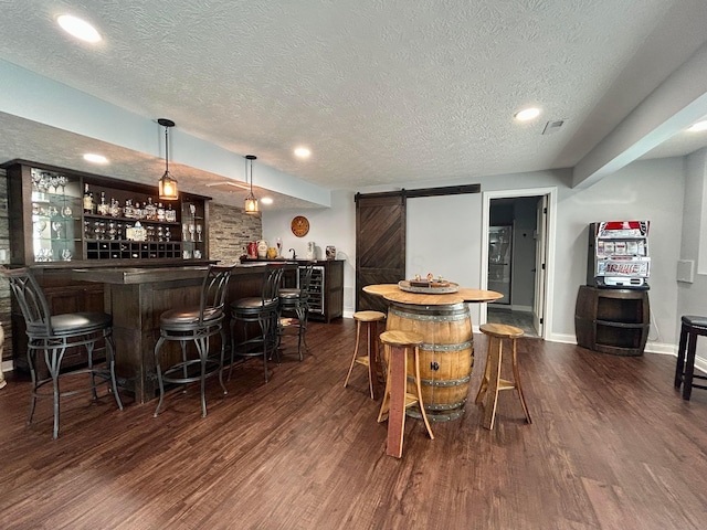 bar featuring a textured ceiling, dark wood-type flooring, a bar, and a barn door