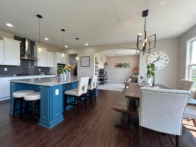 interior space featuring wall chimney exhaust hood, dark wood-style floors, arched walkways, a spacious island, and white cabinetry