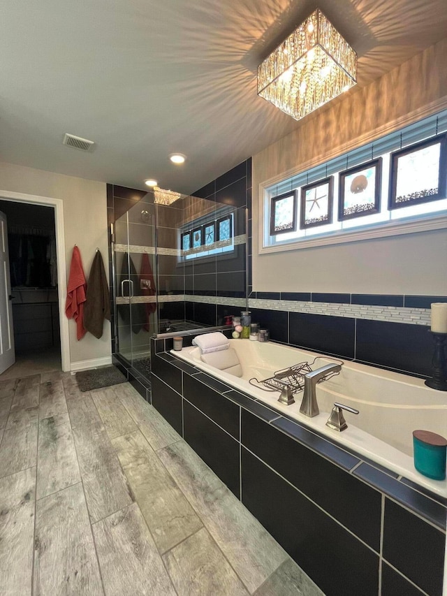full bathroom with a bath, visible vents, an inviting chandelier, wood finished floors, and a shower stall
