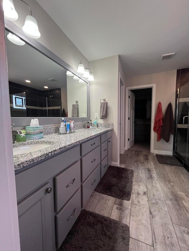 bathroom featuring wood finished floors, visible vents, a sink, and a shower stall