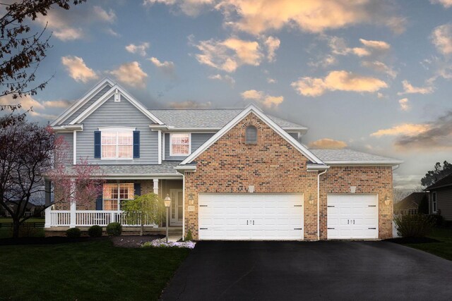 traditional home with a yard, an attached garage, driveway, covered porch, and brick siding