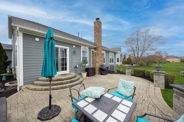 back of house with a chimney, central air condition unit, a patio area, and a shingled roof