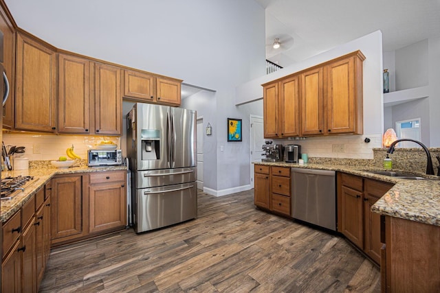 kitchen featuring brown cabinets, backsplash, a sink, dark wood-type flooring, and appliances with stainless steel finishes