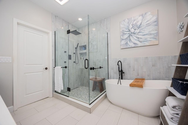 bathroom with a freestanding bath, a stall shower, tile patterned floors, and tile walls