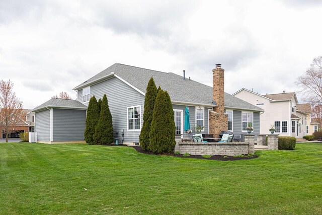 back of house featuring a lawn, a chimney, a patio, and roof with shingles