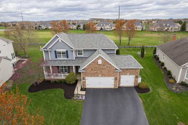 traditional-style house featuring aphalt driveway, fence, a shingled roof, a residential view, and brick siding