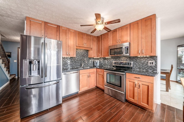 kitchen featuring wood tiled floor, stainless steel appliances, backsplash, a sink, and ceiling fan