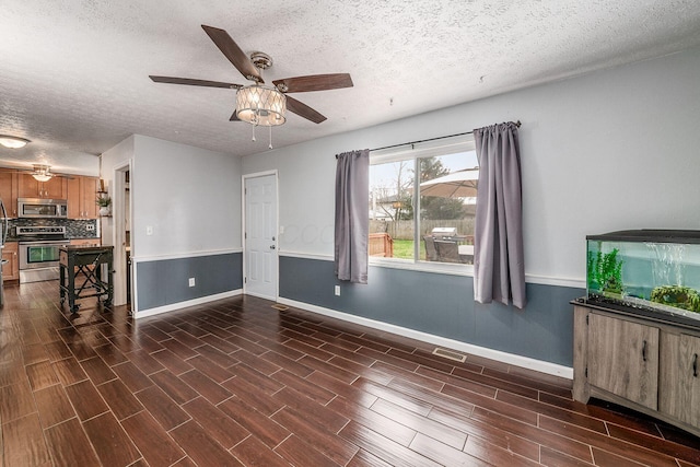 unfurnished living room featuring dark wood-style floors, a textured ceiling, baseboards, visible vents, and ceiling fan