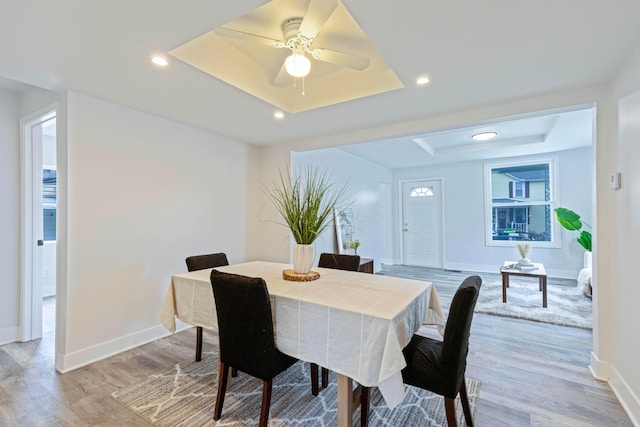 dining room featuring light wood-style flooring, a tray ceiling, baseboards, recessed lighting, and a ceiling fan